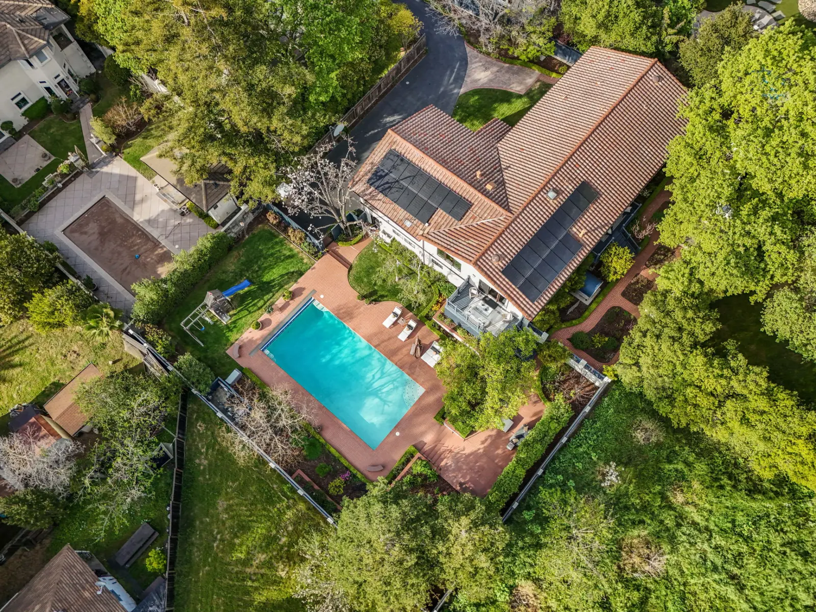Aerial view of the home, pool and gardens surrounded by tall trees