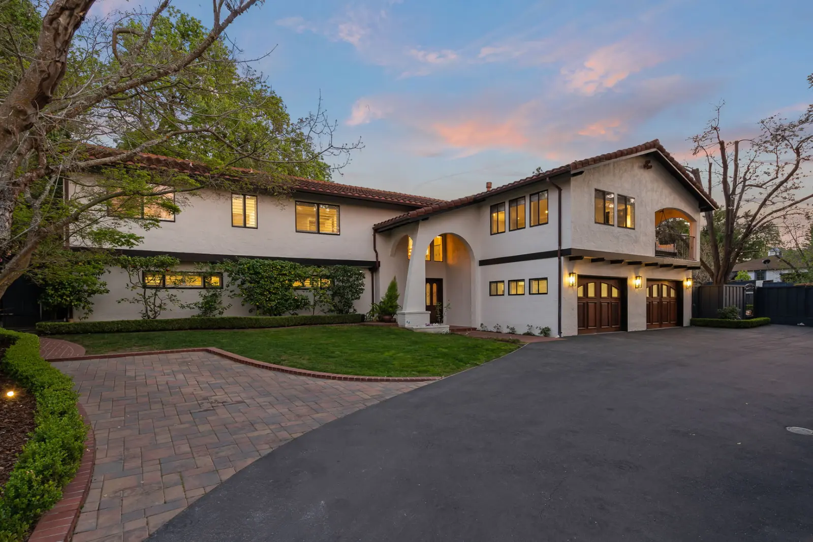 Front of a white stucco home with a tile roof and paver driveway at twilight