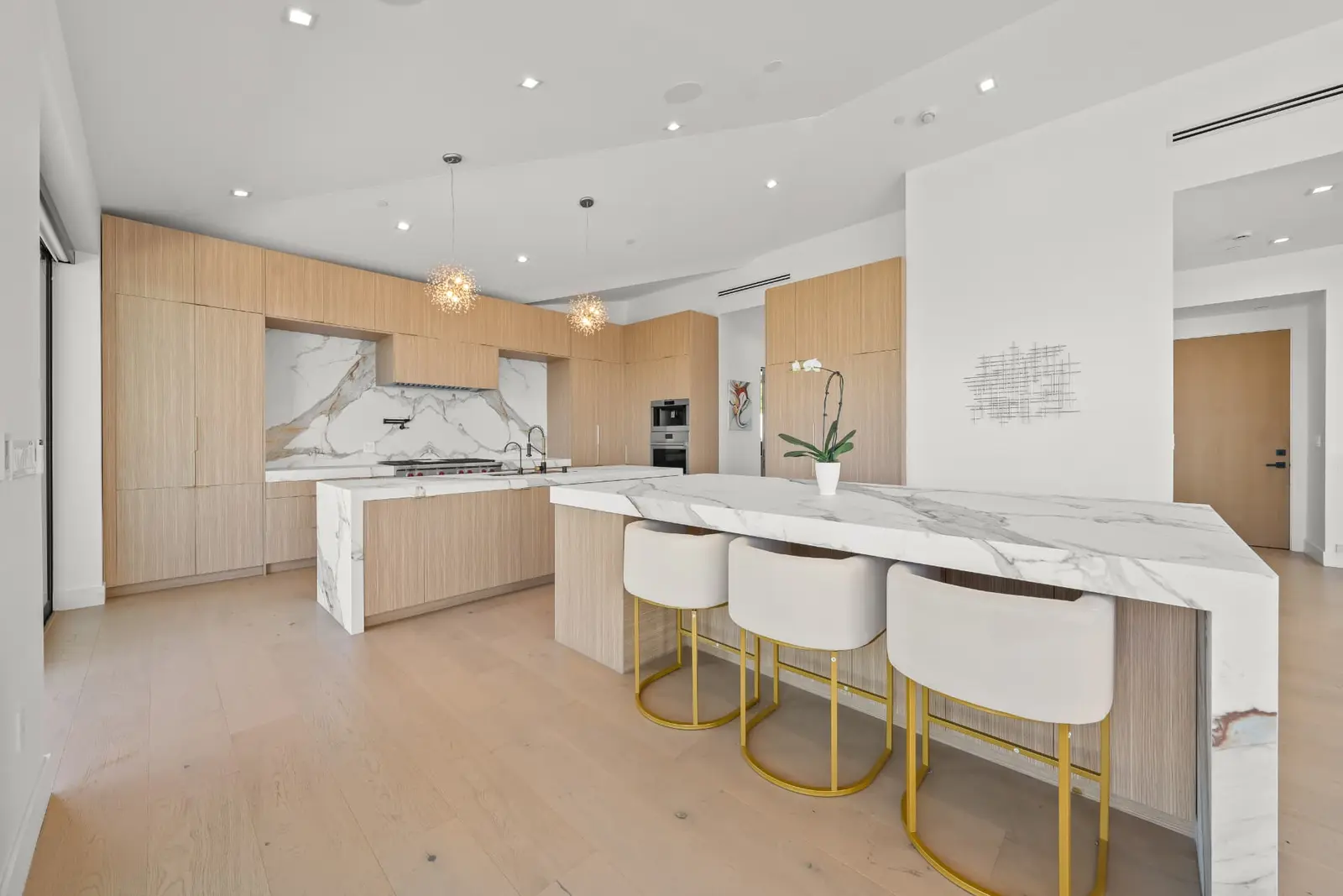 Light oak kitchen with a waterfall marble island and gold barstools