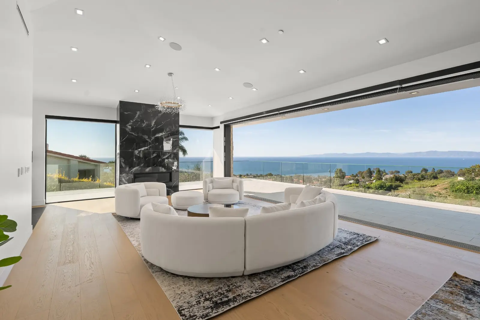 Bright living room with curved white sofas and a wall of glass opening to a Pacific Ocean view
