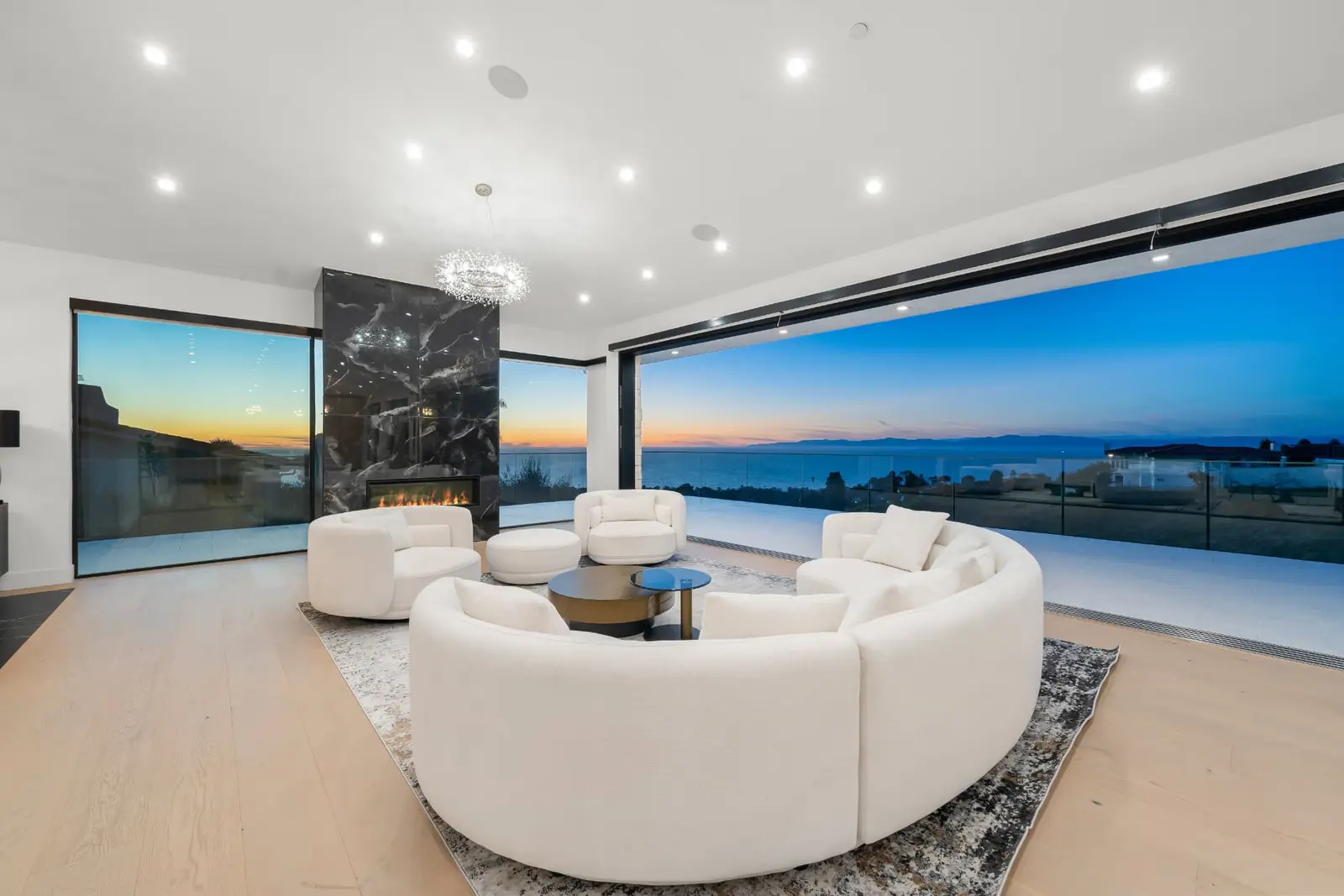 Living room at sunset with curved sofas and a glowing ocean horizon